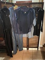 Photo showing multiple women's clothing items including jumpsuits, blouse, dress, and blouse hung on hangers against a folding screen.