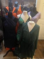 Seven women's dresses displayed on mannequins and hangers including dark blue sparkle strapless dress with fitted bodice and flowing skirt, green dress with V neckline, orange beaded dress, orange sundress, blue printed sundress, and lilac dress.