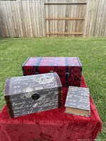 Photo showing the three items together on a red rug outdoors: the medium red storage chest, small Paris design chest, and decorative book.