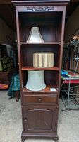 Full view of wood cabinet showing all three lamp shades placed on each shelf and visible wear on cabinet door and shelves.