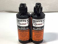 Front view of two black plastic 59ml bottles of Hoppe's Elite Gun Oil with orange and white labels indicating superior lubrication and corrosion protection.
