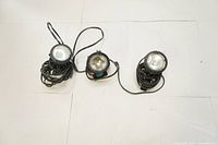 Three mini halogen clamp lights arranged side by side on a light surface, showing front reflectors and cords coiled around bases.