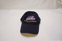 Front of black cotton baseball cap showing embroidered 'Big Daddy's' in purple, white, orange, and yellow