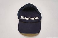 Front view of navy blue Shimano baseball cap showing logo embroidered in white on structured front panel with curved brim.