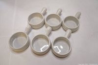 Top view of six white porcelain mini serving dishes with handles, arranged in two rows of three.