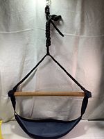 Front view of the rope tree swing hanging, showing triangular black rope, wooden bar and fabric seat.