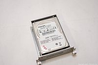 Front view of Toshiba HDD2J96 160GB hard drive mounted in metal bracket, showing label with product details and certification logos.
