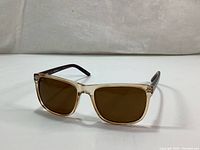 Angle view of the sunglasses showing the side and front of the beige translucent frame and brown lenses.