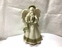 Front view of ceramic angel figurine music box with white and green robes, halo, and wings.