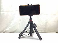 Tripod shown set up with smartphone in horizontal orientation, tripod legs fully extended and supporting phone holder clamp.