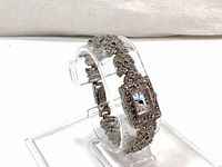 Silver tone ladies bracelet watch with green accents on a clear stand, showing side angle of watch face and band design.