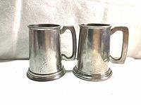 Front and side view of two vintage English pewter tankards with clean surfaces and some patina, showing their shape and handles.