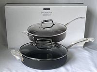 Photo of the brand new Epicure Perfect Pan saute pan with glass lid sitting in front of its box, showing the pan's black ceramic-coated interior, stainless steel handles, and clear glass lid.