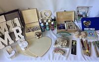 Wide view of the craft supplies lot showing wooden shapes, bottles of paint, paintbrushes, craft stamps, and other materials laid out on a white background.