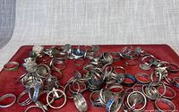 Overhead view showing a large assortment of silver-toned costume rings with various designs, including coin style and enamel inlays.