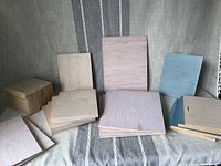 Overview of 27 pine wood blanks in various sizes and styles, showing stacks and individual plaques upright, including some with blue protective layer and beveled edges.