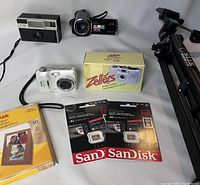 Overview of cameras, cameras accessories, photo paper, memory cards and tripod arranged on white surface