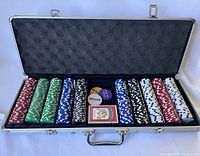 Open poker case displaying poker chips in five colors, two decks of cards, dealer chip, and small blind chip arranged inside foam insert.