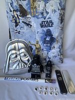 Photo showing Star Wars duvet cover with characters, Darth Vader cake pan, Darth Vader Lego minifigure, Darth Vader Lego alarm clock, Lego pins, and rolled posters.