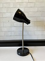 Photo showing the black mid-century modern style adjustable gooseneck lamp with round base and black conical shade, positioned upright and plugged in.