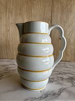 Front side of the ribbed ceramic pitcher vase featuring a scalloped handle and spout with yellow lines accenting the ribs.