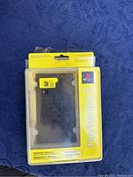 Front view of the sealed PlayStation 2 Network Adapter in original Sony packaging showing the black adapter through clear plastic with Sony branding and text.