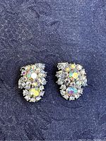 Pair of Trifari clip earrings lying on blue fabric showing detailed multicolored rhinestone cluster design.