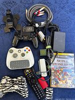 Top down photo showing all items in the lot spread on a blue patterned surface including controllers, cables, remote, and game case