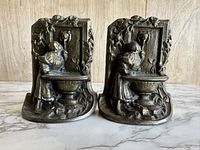Front view of the pair of cast iron bookends featuring a lady at a lion head fountain with floral design borders.