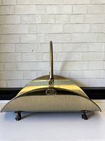 Front view of vintage brass firewood holder with claw feet and central handle.