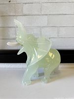 Front and side view of vintage green glass elephant figurine showing trunk raised and detailed carving of ears and legs.