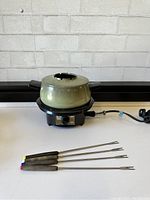 Full view of green ceramic fondue pot with lid on black electric base and power cord
