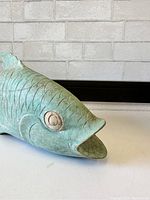 Close-up image focusing on the carved face and upper body of the koi fish sculpture, showing detailed scales and open mouth with green patina finish.