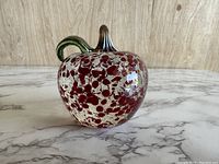 Front view of the glass apple paperweight showing red and white speckled glass and green stem