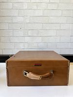 Front view of closed vintage brown leather Travelaire suitcase with handle, showing detailed top stitching and metal fittings.