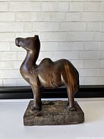 Front view of the hand carved wooden camel statue with natural wood grain and polished finish mounted on wooden base.