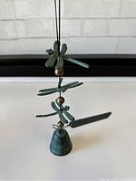 Close-up of the three dragonflies arranged vertically above the small bell with green patina finish.