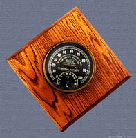 Square wooden plaque with round black dial hygrometer and thermometer, showing wood grain and brass bezel.
