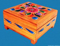 Side angled view of square wooden trinket box showing colorful hand painted floral design on lid and blue painted accents on sides; box stands on short legs.