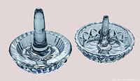 Two glass jewelry trays/ring holders with clear intricate cut glass patterns, one with a thick central cone and the other with a taller slender cone.