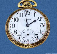 Front view of the pocket watch showing white dial with black Arabic numerals, red minute dots, and sub-seconds dial. Gold ornate crown and bezel visible.