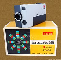 Front and side view of Kodak Instamatic M4 movie camera resting on its original box showing branding and lens.