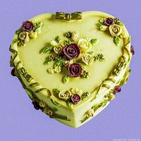 Top-down view of the heart-shaped trinket box showing detailed hand-painted flowers and gold ribbon accents on a pale yellow background.
