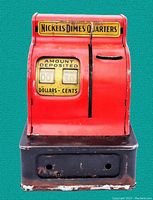 Front view showing red tin cash register bank with mechanical amount display and black base with paint chipping.