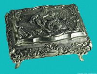 Front angled view highlighting the detailed repousse metalwork on the hinged lid and the ornate footed base of the small box.