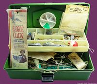Open green tackle box showing internal compartments filled with a variety of fishing tackle including vintage Eagle Claw fish hooks, bobbers, and sinkers.