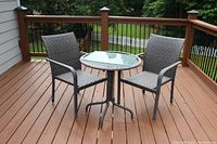 Two gray woven rattan outdoor chairs and one round patio table with glass top on a wooden deck.