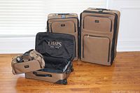 Four pieces of Chaps luggage: three upright rolling suitcases in tan with black trim and one matching duffel bag displayed on a wood floor against a white background