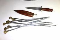 Full view of the dagger, sheath, and six barbecues skewers with coin handles arranged on a white background.