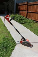 Full view of BLACK+DECKER electric string trimmer with handle, pole, and 2-in-1 wheeled attachment on concrete path and grass.